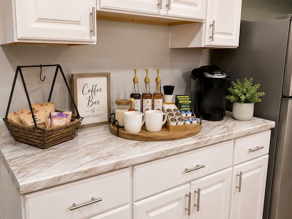 A kitchen counter with a coffee bar setup including a basket, coffee mugs, a Keurig coffee maker, and a potted plant.