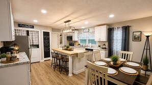 Una cocina moderna con una isla central, armarios blancos y un comedor con sillas de madera y una mesa oscura.