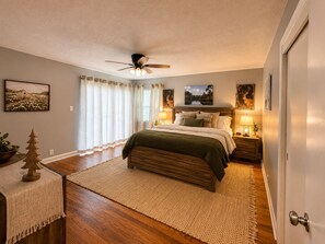 A bedroom with a bed, bedside lamps, a ceiling fan, and artwork on the walls.