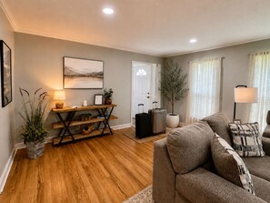 Una sala de estar con un sofá, una mesa de centro de madera, una lámpara y una planta en maceta.