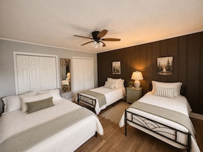 A bedroom with two beds, a ceiling fan, a nightstand with a lamp, and a mirror.
