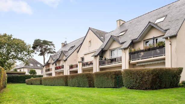 A row of residential buildings with sloped roofs, balconies, and a well-maintained lawn.