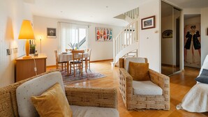 A spacious living area with wicker furniture, a dining table, and a staircase leading to another level.
