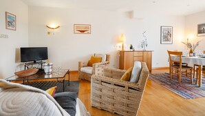 A living room with a TV, wicker furniture, a dining table with chairs, and wall-mounted lights.