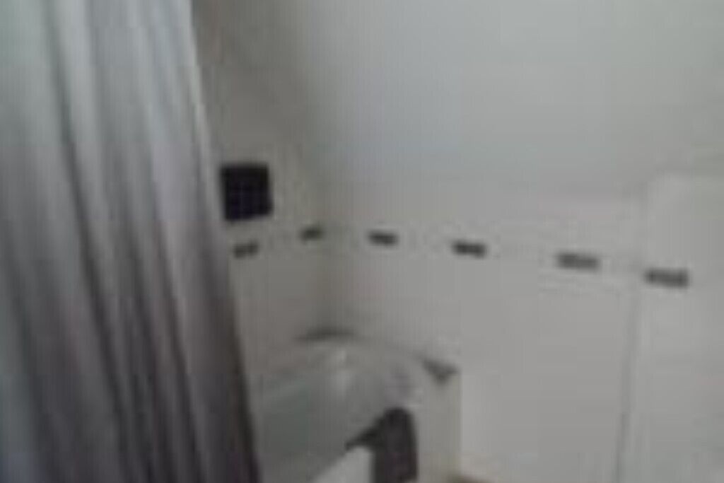 Un pasillo estrecho con una puerta blanca a la izquierda y una pared blanca con un pequeño ventanal a la derecha.