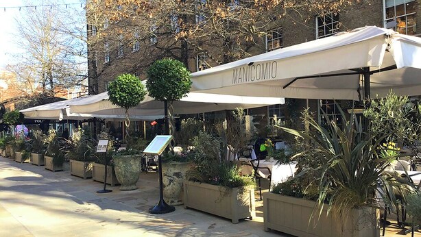 Une rangée de parasols d’extérieur, arborant le logo « MANICOMIO », des plantes en pot et un ciel dégagé.