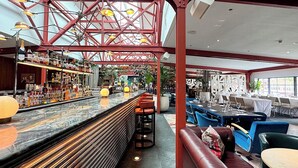 Un espace bar doté d’un long comptoir, de tabourets et d’une structure métallique rouge au-dessus.