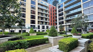 Un immeuble moderne à plusieurs étages, doté de balcons, et entouré de jardins et de haies bien entretenus.