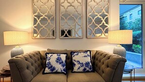 Un canapé capitonné agrémenté de deux coussins décoratifs, flanqué de deux lampes, et surmonté de trois panneaux décoratifs fixés au mur.