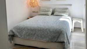 Ein modernes Schlafzimmer mit einem Bett, einer Nachttischlampe, einem kleinen Hocker und zwei gerahmten Bildern an der Wand.