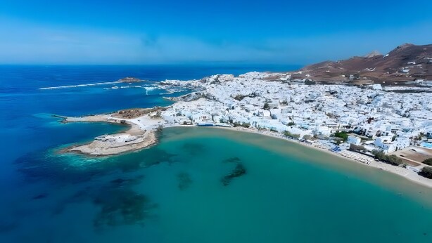 Luftaufnahme einer Küstenstadt mit weißen Gebäuden, einem Strand und klarem türkisblauem Wasser.