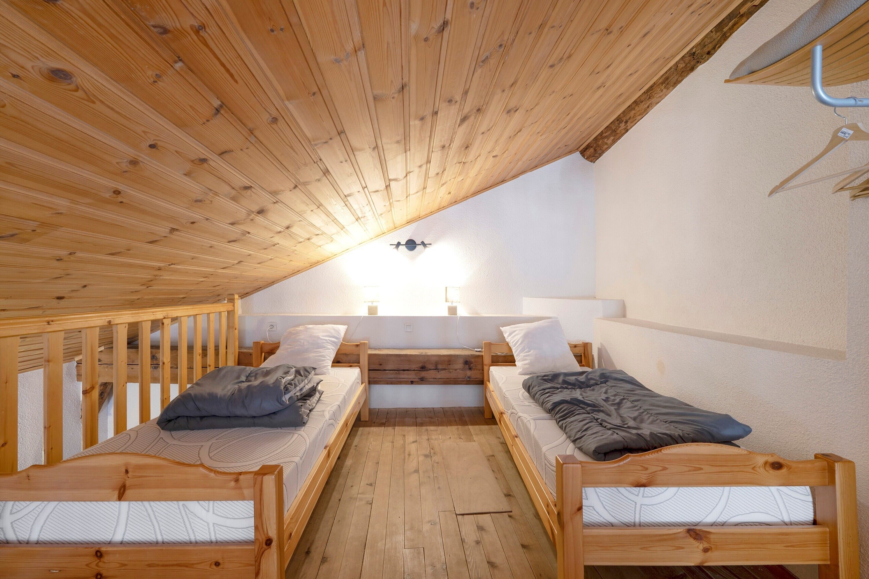 Een kamer met houten stapelbedden, een schuine balkenkap en een lamp.