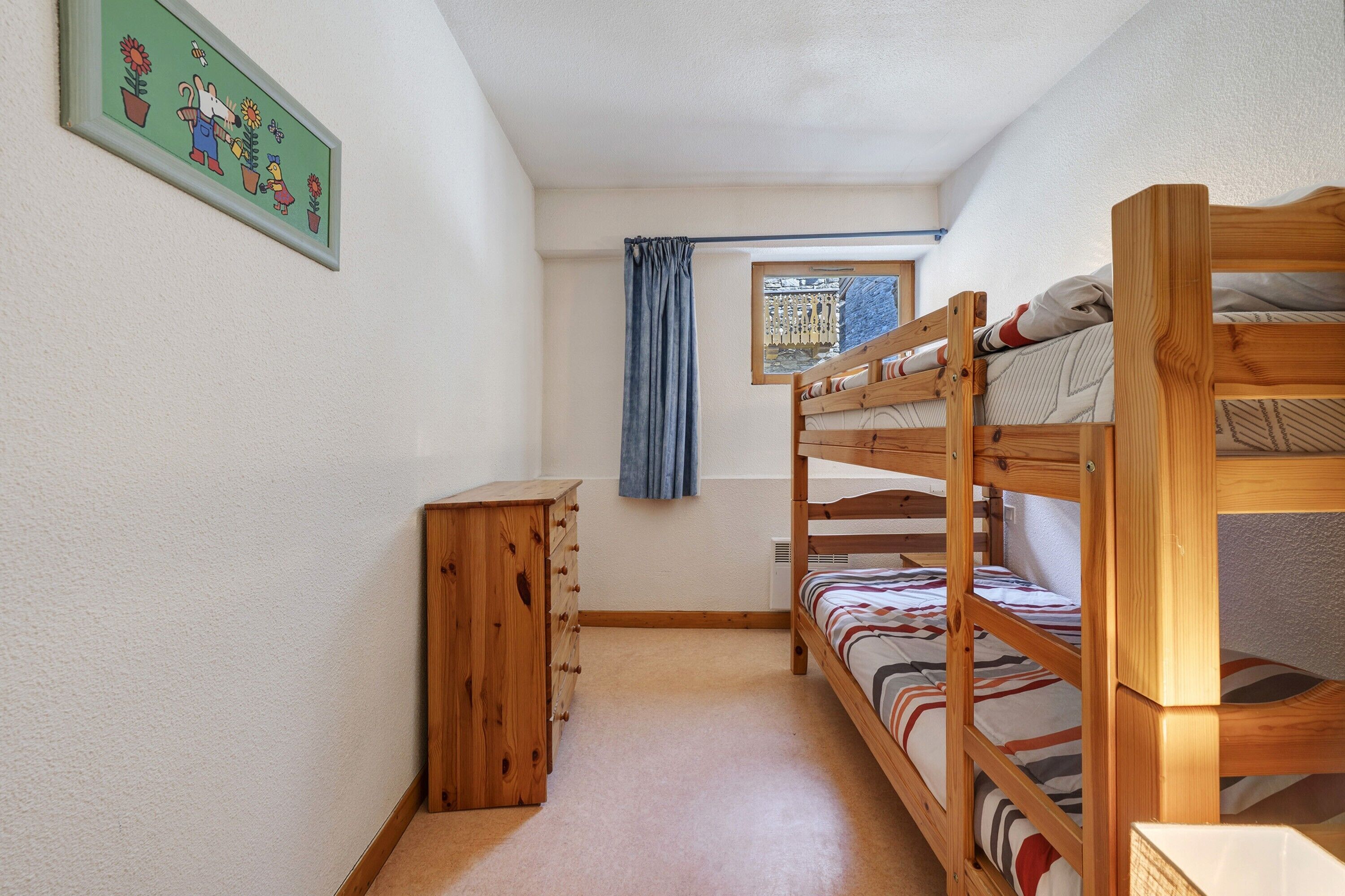 A bunk bed room with a wooden dresser, a window with curtains, and a wall-mounted picture.