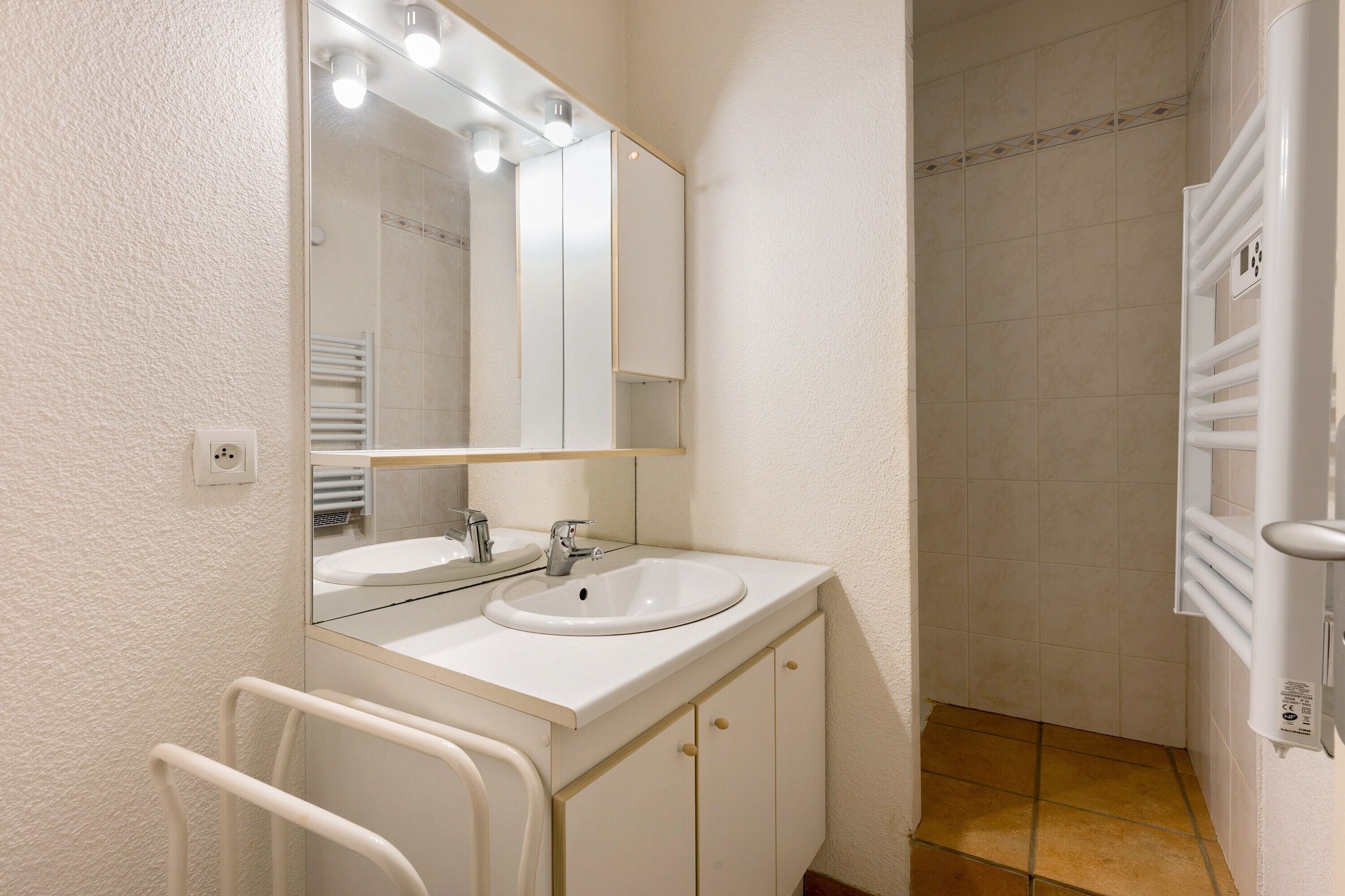 A bathroom with a sink, mirror, towel rack, and shower.