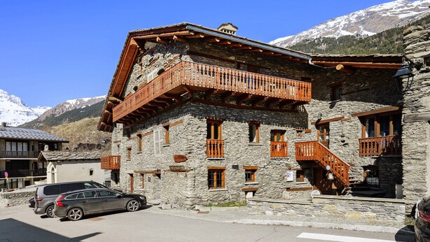 A stone building with wooden balconies and a car parked in front. - Apartment 'Les Gentianes' with Mountain View and Wi-Fi (Val-Cenis)