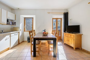 Une cuisine compacte comprenant une table à manger, des chaises, un téléviseur posé sur un meuble en bois et une fenêtre avec des rideaux.