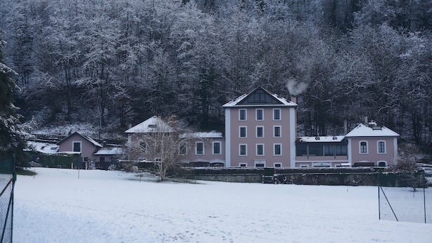 Un edificio grande de varios pisos con una torre central, rodeado de árboles cubiertos de nieve.