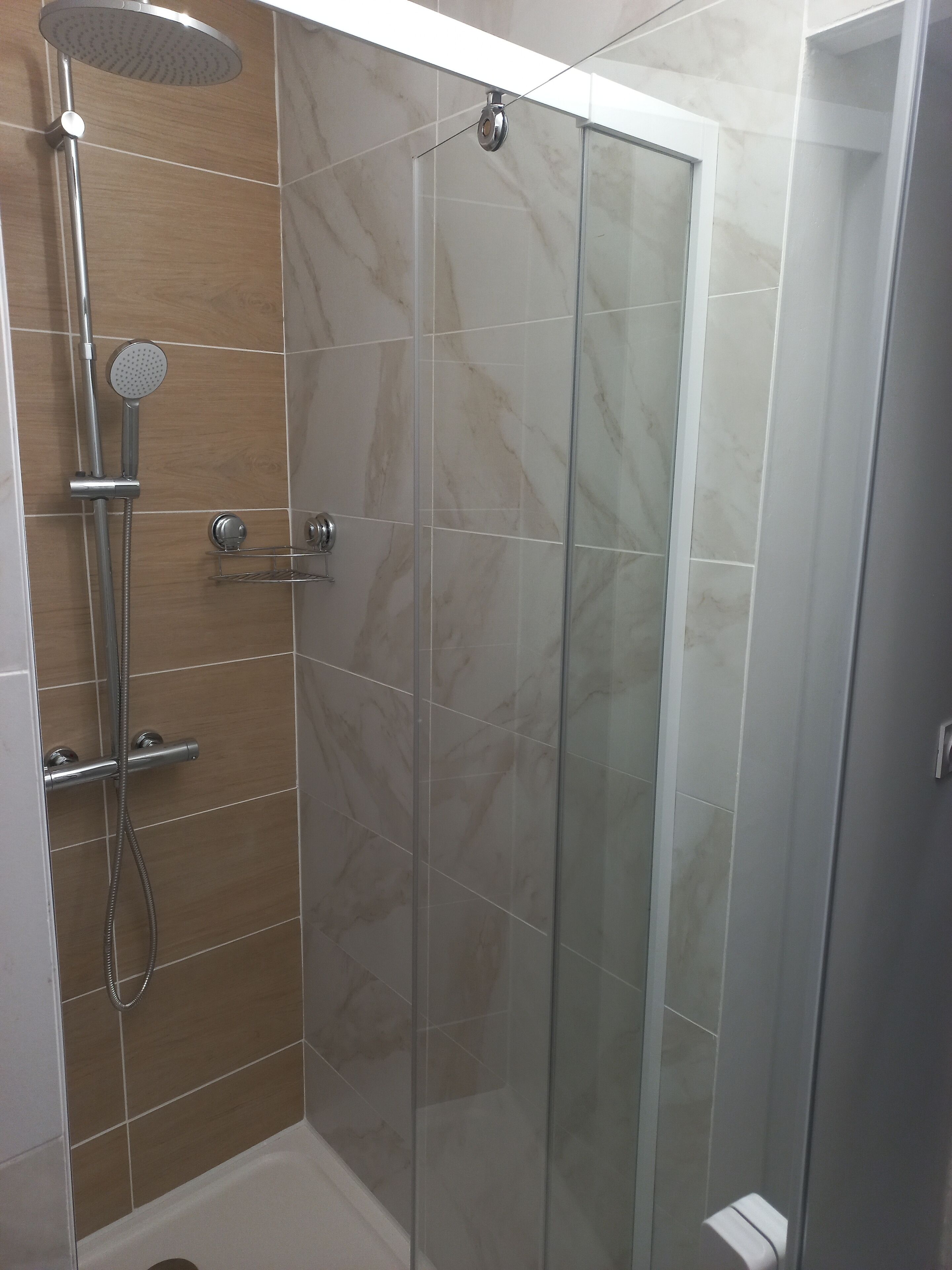 A modern shower enclosure with a glass door, a handheld showerhead, and a wall-mounted faucet.