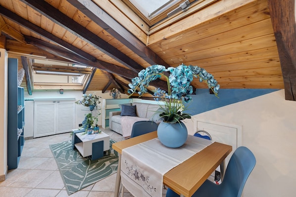 Une pièce mansardée chaleureuse avec un plafond en bois, une table à manger avec des chaises, un canapé et une plante en pot.