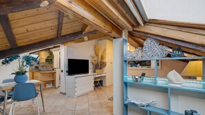 Una habitación acogedora y bien iluminada con techo de madera, televisión, escritorio y una silla azul.