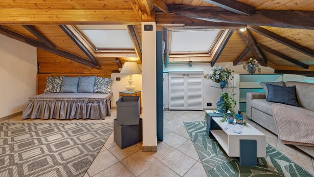Un dormitorio estilo loft con techo inclinado, tragaluces, una cama, un sofá, una mesa de centro y una mesita con una lámpara.