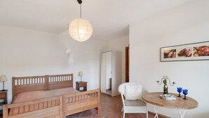 A bedroom with a wooden bed, a round table with two blue cups, a white chair, and a wall-mounted picture. - Holiday Home 'Casa Bilger' with Sea View, Private Terrace and Wi-Fi (Dolcedo)