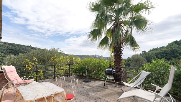 A wooden deck with a table and chairs, a grill, and a palm tree. - Holiday Home 'Casa Bilger' with Sea View, Private Terrace and Wi-Fi (Dolcedo)