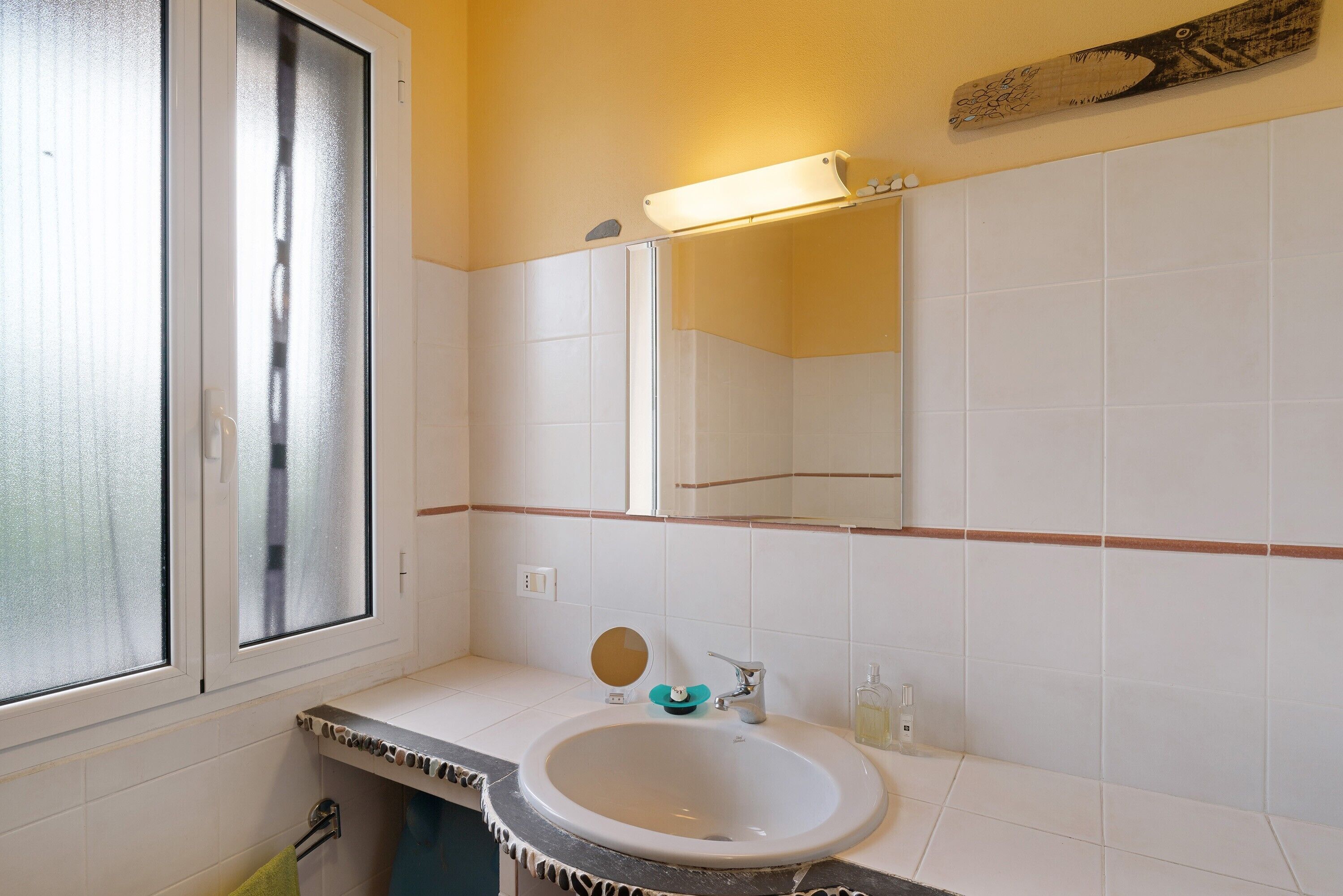 Une salle de bain avec un lavabo blanc, un miroir, une fenêtre et un porte-serviettes.