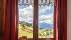 A window with red curtains, a wooden frame, and a view of a mountainous landscape with a fence and buildings. - Apartment 'Appartamento Pila Vacanze' with Mountain View, Shared Garden and Wi-Fi (Gressan)