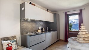 A modern kitchen with grey cabinets, a stainless steel range hood, and a window with a view of mountains. - Apartment 'Appartamento Pila Vacanze' with Mountain View, Shared Garden and Wi-Fi (Gressan)