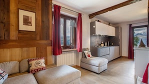 A cozy room with a sofa, a small table, and a kitchen area with a window. - Apartment 'Appartamento Pila Vacanze' with Mountain View, Shared Garden and Wi-Fi (Gressan)