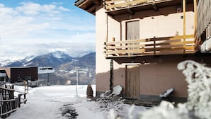 A snow-covered outdoor area with a wooden fence, a chair, and a building with a balcony. - Apartment 'Appartamento Pila Vacanze' with Mountain View, Shared Garden and Wi-Fi (Gressan)