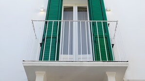 A building with white walls, green shutters, and a balcony with a metal railing.