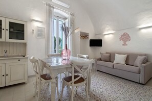 Un comedor con una mesa y sillas, un sofá, un televisor montado en la pared y una ventana con cortinas.