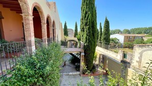 A courtyard with a brick archway, a stone bridge, and tall cypress trees. - Apartment 'Apartaments Can Gibert - Aiguamolls' with Private Terrace, Wi-Fi and Air Conditioning (Castelló d'Empúries)