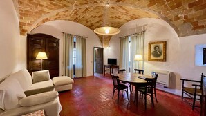 A room with a dining table, chairs, a sofa, a television, and a painting on the wall. - Apartment 'Apartaments Can Gibert - Aiguamolls' with Private Terrace, Wi-Fi and Air Conditioning (Castelló d'Empúries)