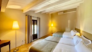 A hotel room with two beds, a desk, a lamp, and a window with blinds.