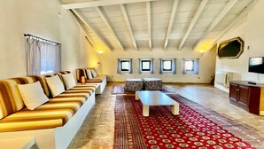 A spacious living room with a high ceiling, a sofa set, a coffee table, a TV, and a patterned rug.