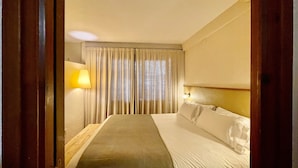 A hotel room with a bed, curtains, a lamp, and a window.