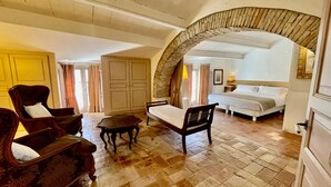 Ein Zimmer mit einem Bett, einer hölzernen Bank, einem Stuhl und einem Steingewölbe.