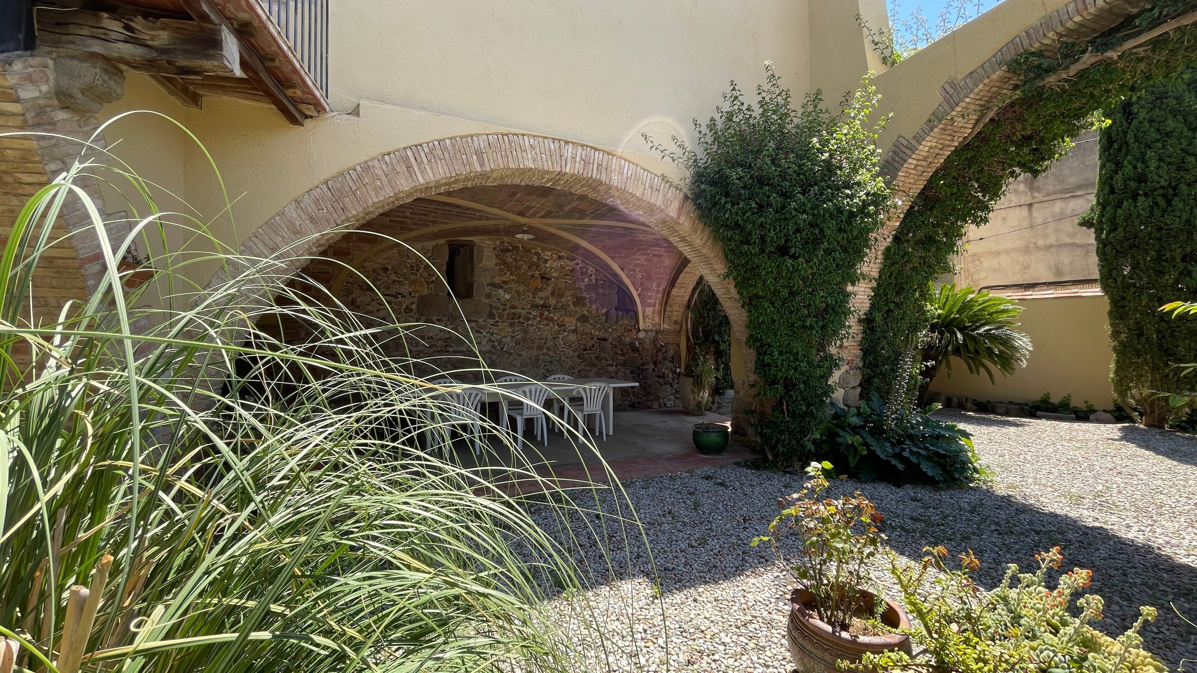 Un patio al aire libre con arcos de piedra, sillas blancas y plantas en macetas.