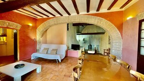 A cozy room with a sofa, a dining table, and chairs, an arched doorway, and a fireplace. - Apartment 'Apartaments Can Gibert - Muralla' with Shared Garden, Balcony and Wi-Fi (Castelló d'Empúries)