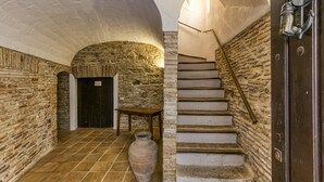 A stone-walled corridor with a tiled floor, a wooden table, a large vase, and a staircase with a metal handrail. - Apartment 'Apartaments Can Gibert - Muralla' with Shared Garden, Balcony and Wi-Fi (Castelló d'Empúries)