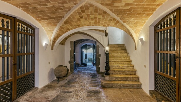Un pasillo con suelo de piedra, techos abovedados y puertas de madera.