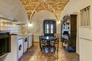 A kitchen with a brick ceiling, a round table with chairs, a washing machine, and a refrigerator.