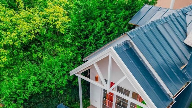 Une terrasse en bois avec une piscine, un petit bâtiment blanc doté d’un toit en pente, et une végétation luxuriante tout autour.