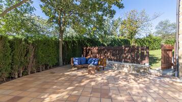 Un patio con un banco de madera y un sofá, rodeado por un seto y árboles.