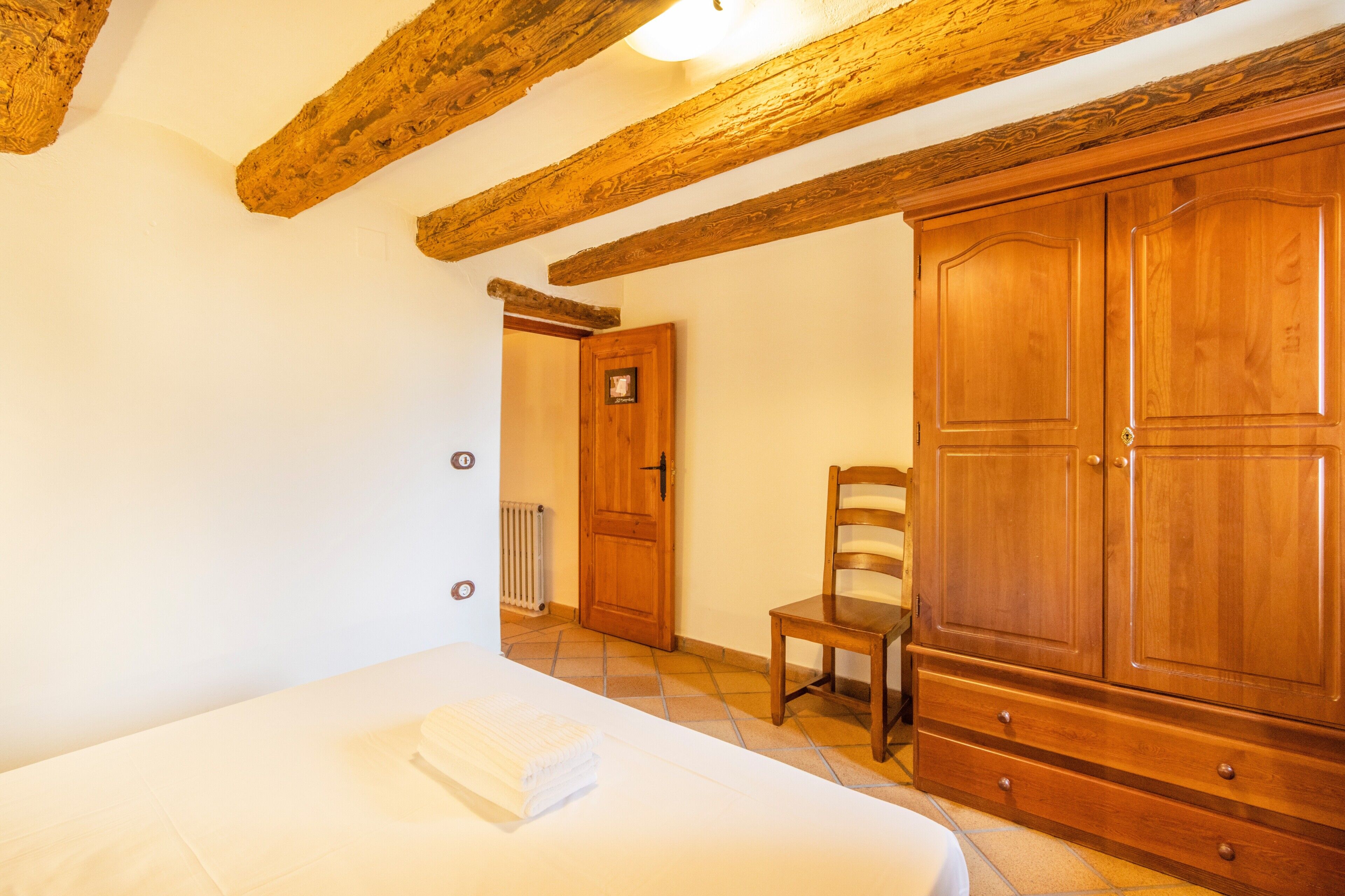 A bedroom with a bed, wooden wardrobe, and a chair.