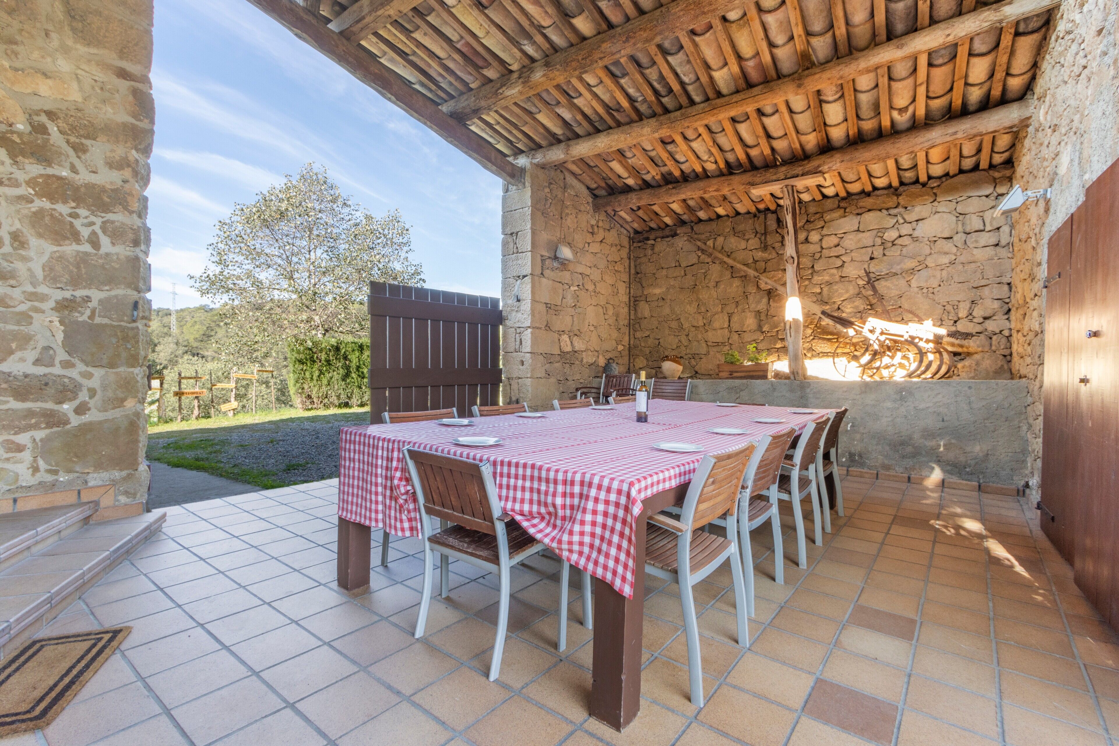 Un patio al aire libre con una pared de piedra, piso de baldosas y una mesa con mantel a cuadros y sillas.