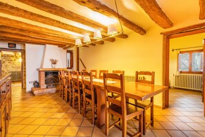 Ein Essbereich mit einem langen Holztisch, Stühlen, einem Kamin und freiliegenden Holzbalken an der Decke.
